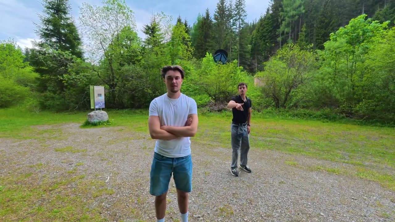 Standbild aus dem Intro: Jonas und Levin stehen auf einer Kiesfläche vor bewaldeten Berghängen